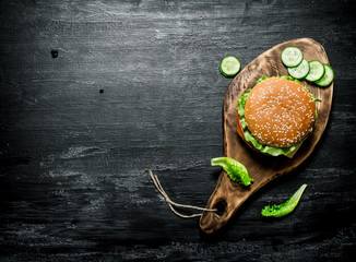 Burger on a cutting Board with cucumber and herbs.