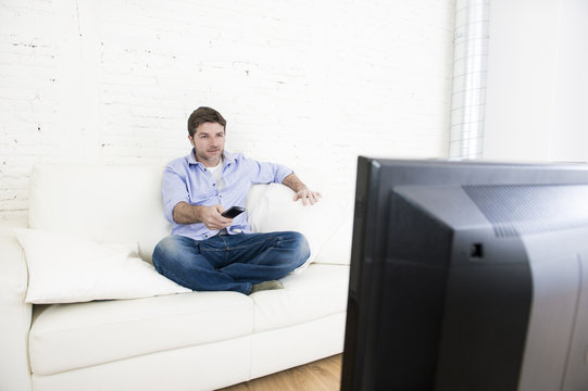 young happy man watching tv sitting at home living room sofa looking relaxed enjoying television