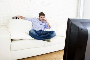 young happy man watching tv sitting at home living room sofa looking relaxed enjoying television