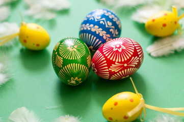 Easter colourful eggs with feathers on green background. Colourful painted eggs – red, blue, green and yellow. Matte background.