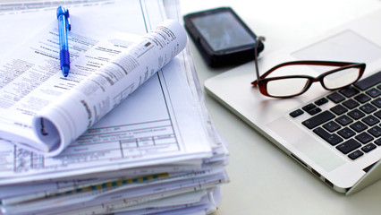 Laptop with stack of folders on table on white background