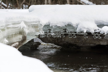 Unique ornamental ice formations hang from an snow-covered ice shelf over a flowing river in northern Wisconsin.