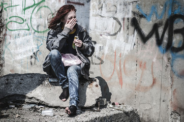 young girl in old dirty ragged clothes, no shoes sitting on a rock, and debris scattered around...