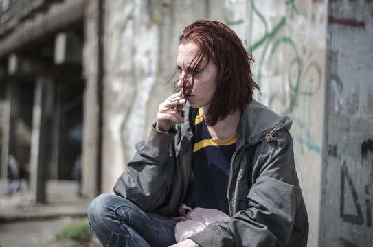 Portrait Of A Young Girl In An Old Dirty, Ragged Clothes With Dirty Hair, Smoking A Cigarette. Disadvantaged Teenager. Homeless Girl.