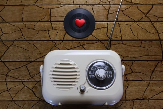 Vintage radio with a vinyl record and a red live heart on a cracked wooden background