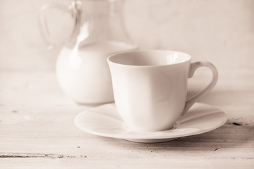 Coffee cup with  blurred jug of milk on the white table