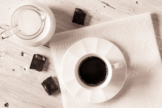 Cup of coffee with jug of milk and chocolate on the white table top view