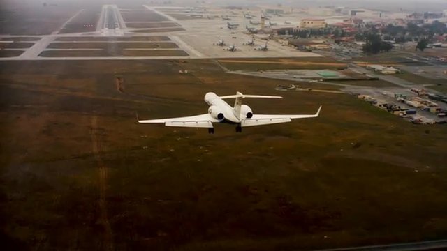 Aerial of a private jet landing at an airport, from behind.