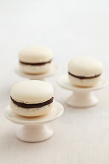 Three white macarons with chocolate buttercream filling on cake stands