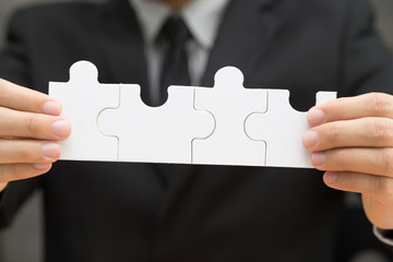 Businessman holding four jigsaw to connect