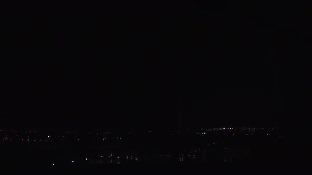 Lightning strikes at night over a distant city.