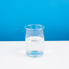 Half empty or half full glass of water on white table. (For positive thinking when see the glass is half full.)