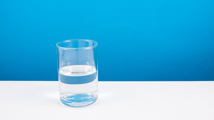 Half empty or half full glass of water on white table. (For positive thinking when see the glass is half full.)