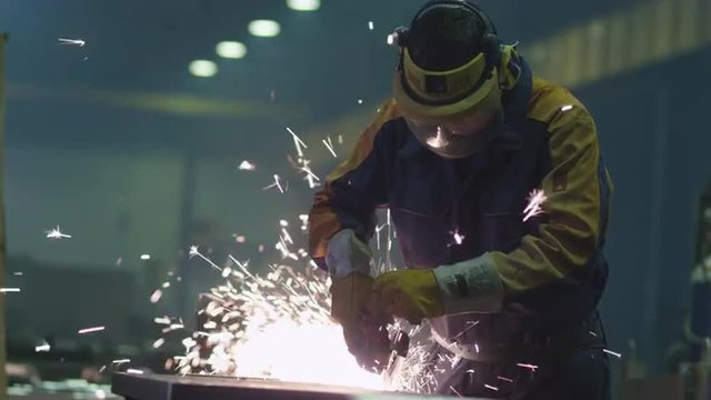 Heavy industry worker at a factory is working with metal on a angle grinder while hot sparks are produced in a result. Shot on RED Cinema Camera.