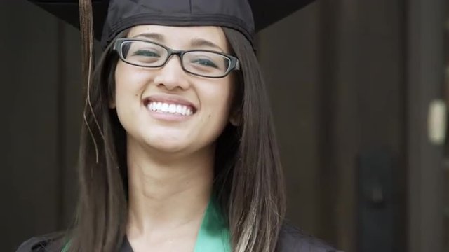 Young woman, in a graduation cap and gown, adjusting her hair.