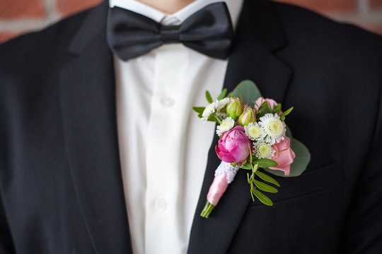 Close up of  white and pink rose corsage. Beautiful boutonniere pinned on man in black suit, white shirt and black bowtie. Groom or graduate.