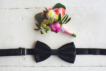 Close up of man accessories. Black bowtie and flower boutonniere on white wood rustic background....