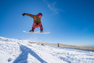 Naklejka na ściany i meble Snowboarder jumping against blue sky