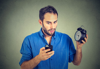 perplexed business man with alarm clock looking at smart phone
