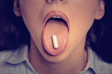 Obraz premium Closeup cropped image of young woman with white pill on her tongue