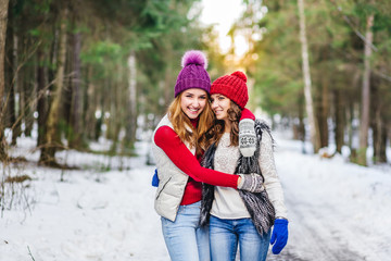 Two girls walking in winter forest. emotional portrait of stylish portrait of pretty young hipster blonde and brown woman,get smile,pink hat,soft colors,cool crazy girl
