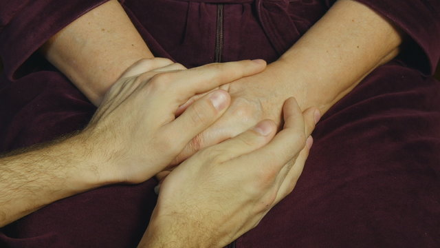 Male hand comforting an elderly pair of hands. 