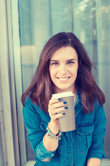 Smiling woman drinking coffee outdoors holding paper cup