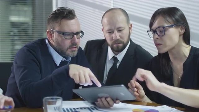 Group of employees are having a conversation in meeting room. Businessman is using a tablet computer. Shot on RED Cinema Camera.
