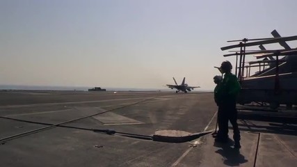 Various jet aircraft land on the deck of an aircraft carrier.