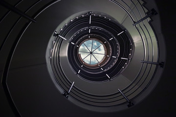 Spiral staircase.Bottom straight up view of a dark spiral staircase with a sky at the top end.