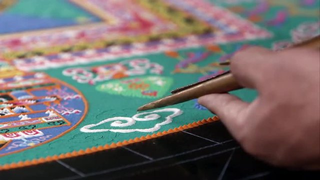 Tight shot of someone adding sand to a colorful sand mandala.