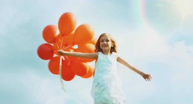Girl in a white dress holding red balloons and spinning against the sky. Sunlight 