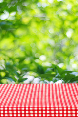 Empty table with red tablecloth over blur garden and bokeh backg