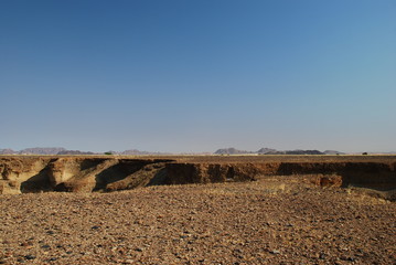 Stony desert plane broken by canyon and mountains in the background