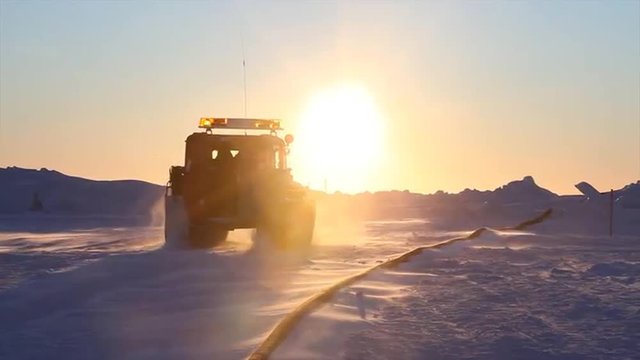 A tundra buggy drives across an ice floe to approach a ship.