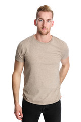 A trendy and attractive man in his 20s wearing black jeans and a tan tshirt standing against a white background in a studio.