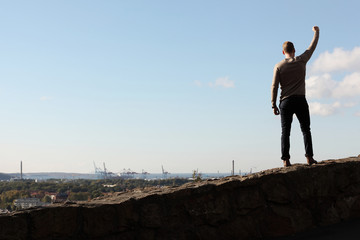 A lonely man standing on top of a wall with a great view of the city in front of him. A sunny summer day with blue sky with clouds.