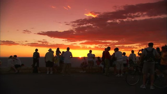 Tourists pause at the rim of the Grand Canyon at sunset.