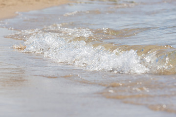 A small sea wave rolls on sandy beach, close-up