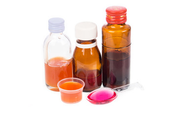 Syrup Medication Bottles and Medicine in Spoons on white backgro