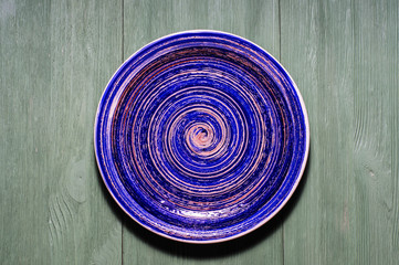 Blue pottery glazed plate on wooden background.