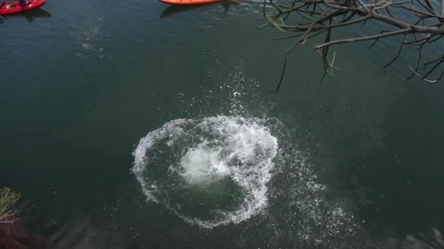 Young white guy jumping from rock face into river below creating a splash.