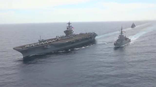 Aerial shots over aircraft carrier and other Navy craft on the sea.