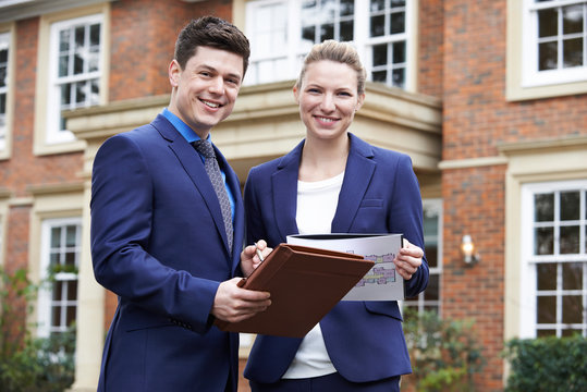 Male And Female Realtor Standing Outside Residential Property
