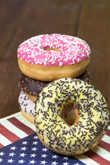 American donuts are stacked on each other and are lying on a napkin  with the design of the American flag. One donut is leaning against the other. 