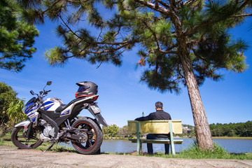Young man sitting alone on park bench, under a willow tree, looking down to the water. LAM DONG, VIET NAM