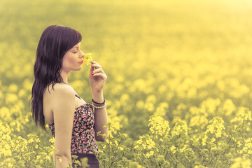 Schöne junge glückliche Frau in der Sonne riecht an gelber Blume. Attraktives Mädchen schnuppert an Blumen auf einer Wiese bis zum Horizont im Sonnenschein im Frühling oder Sommer. Foto einer Serie.