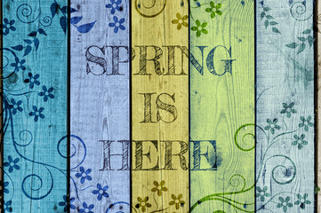 Spring is here written on colourful wooden background