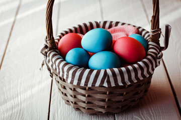 Multicolored Easter eggs in wicker basket on white wooden background