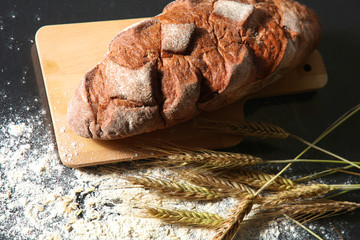 rustic crusty bread and wheat ears on a dark wooden table